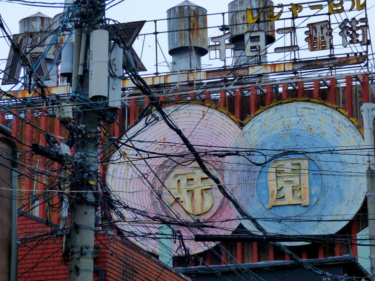 A utility pole with countless cables spanned through the air in front of a large neon advertisement