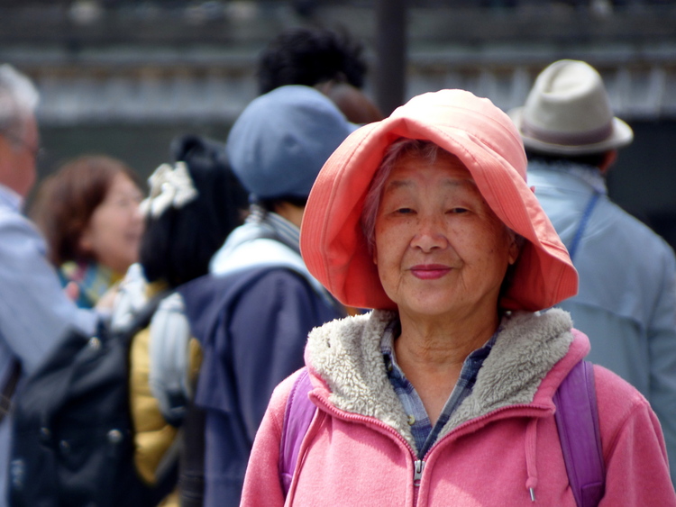 An old woman wearing a pink sweater and salmon fishing hat standing in front of a crowd