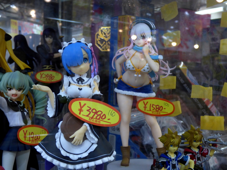 A display of Anime-style figurines, most of them female, with varying amounts of clothing. The figure in front is wearing a French-style maid outfit and has a price sticker reading '¥3980'