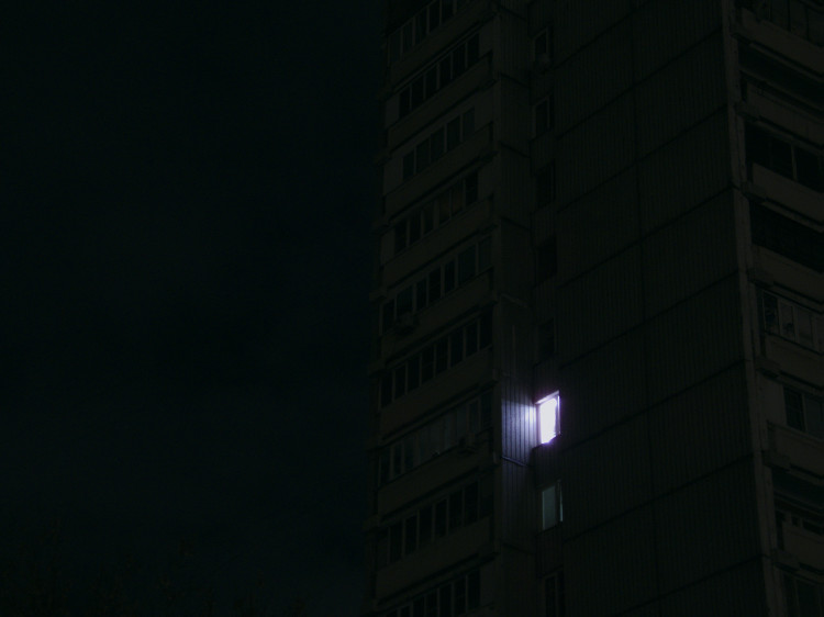 A single illuminated window in a concrete high-rise residential complex at night