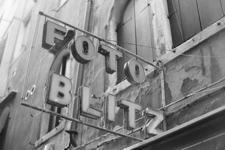An old light-up sign made up of individual boxy letters reading "FOTO BLITZ" mounted on a building facade