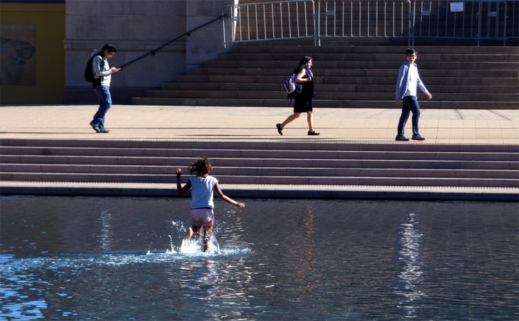 A girl running through a shallow decorative pool on a public square