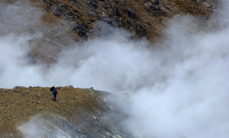 Two tiny figures standing on a mountain ridge surrounded by white volcanic vapour