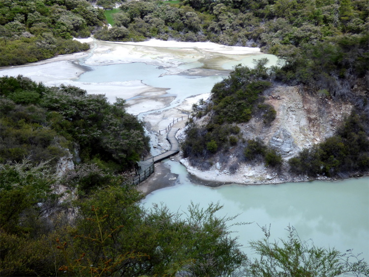 Panorama showing a small bridge over a channel connecting two geothermal pools with milky-white water