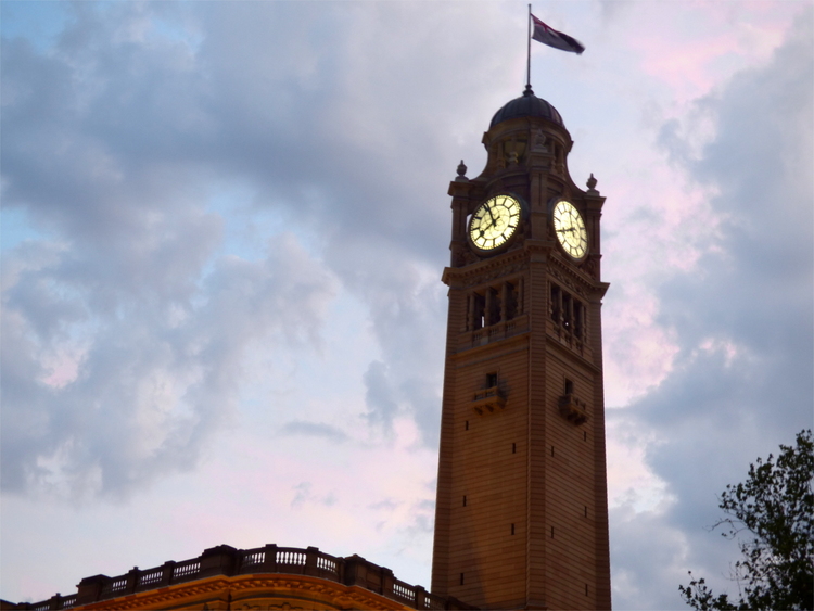 An old clock-tower with a flag waving on top against cloudy evening sky