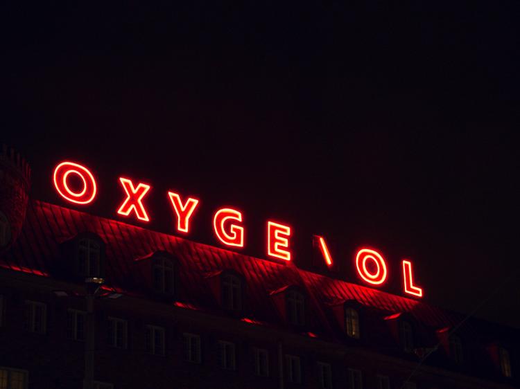 A red neon sign on a rooftop at night reading 'Oxygenol', with the 'N' partially broken