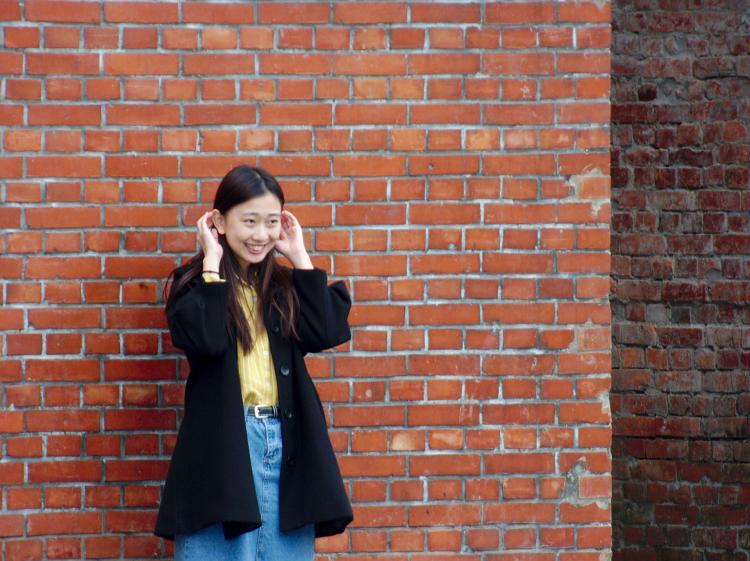 A young woman in a yellow shirt smiling and posing for pictures in front of a red brick wall
