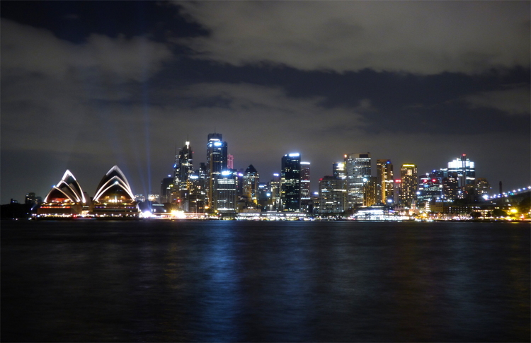 The skyline of Sydney from across the harbour at night, showing the outlines of the Sydney opera house