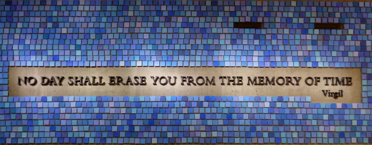 A mosaic-like wall covered in blue square tiles of different shades with an empty space in the middle reading 'No day shall erase you from the memory of Time - Virgil'