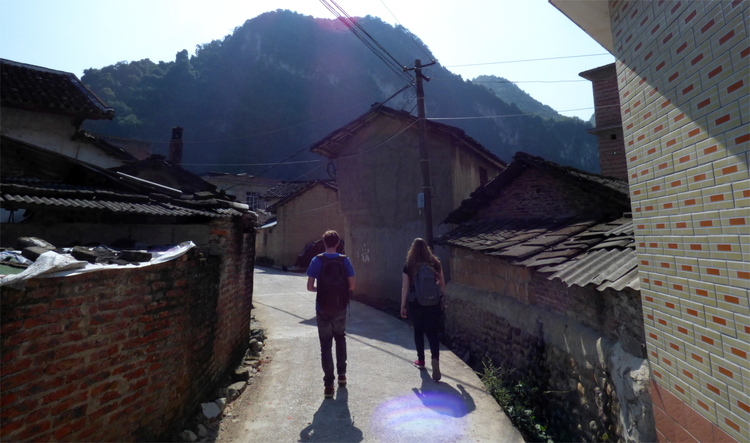Jan and Katha walking away from the camera on a small road leading through a village with brick walls and short, tile-roofed houses