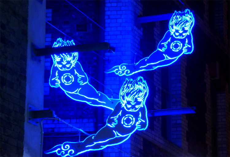 Three transparent, glowing blue signs showing what appear to be wind spirits looking like children suspended from a wall