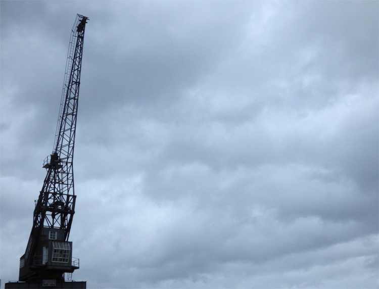 A single, apparently abandoned loading crane standing upright against a cloudy grey sky