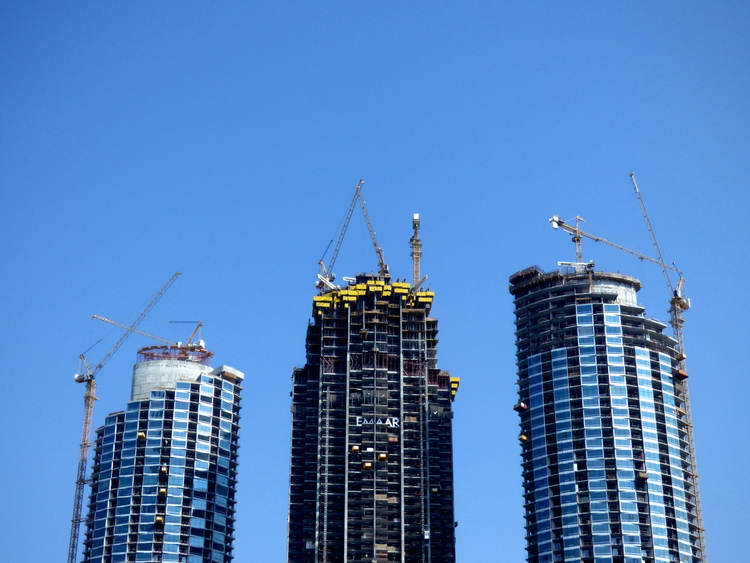 Three high-rise buildings under construction with cranes attached to them