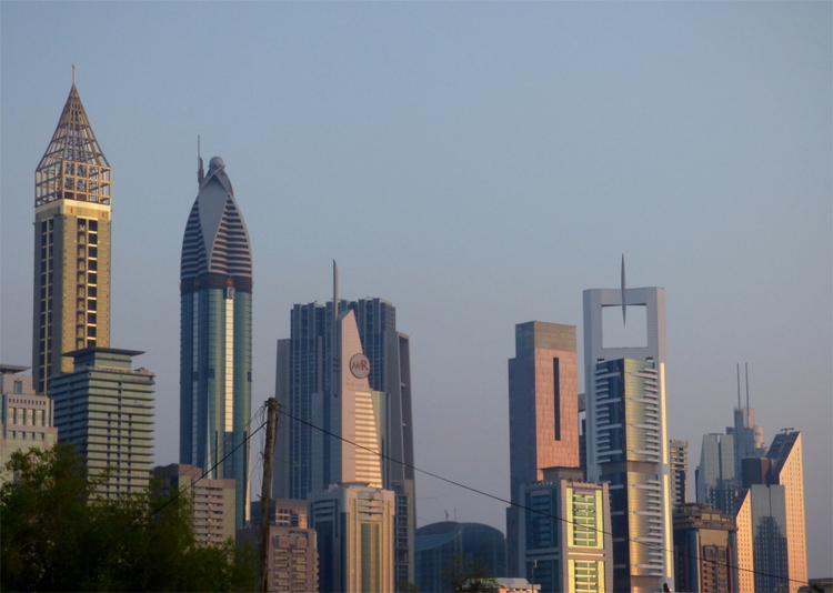 The skyline of Dubai, consisting of several futuristic looking, metallic skyscrapers reflecting the red tones of the evening sun