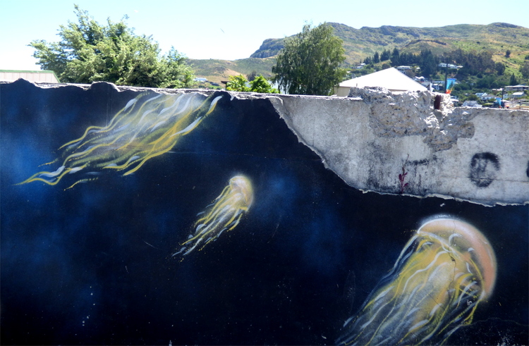 Chipped street-art on a low wall showing yellow jellyfish swimming towards the surface in dark blue water