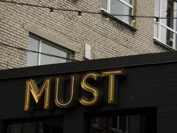 A metal-and-neon sign reading 'Must' on a black building facade