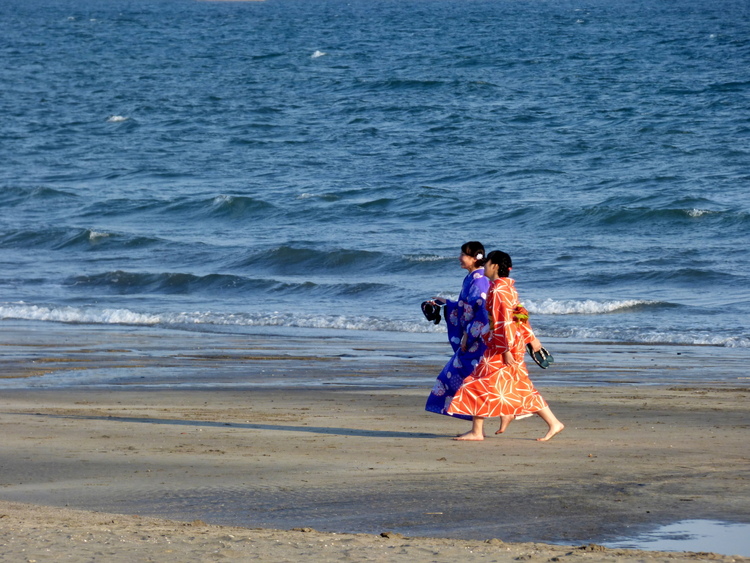 Two women in orange and purple Kimonos walking along the shore