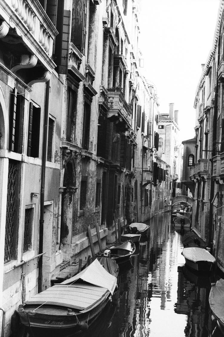 A narrow, back-alley canal between two rows of houses with small boats anchored on both sides
