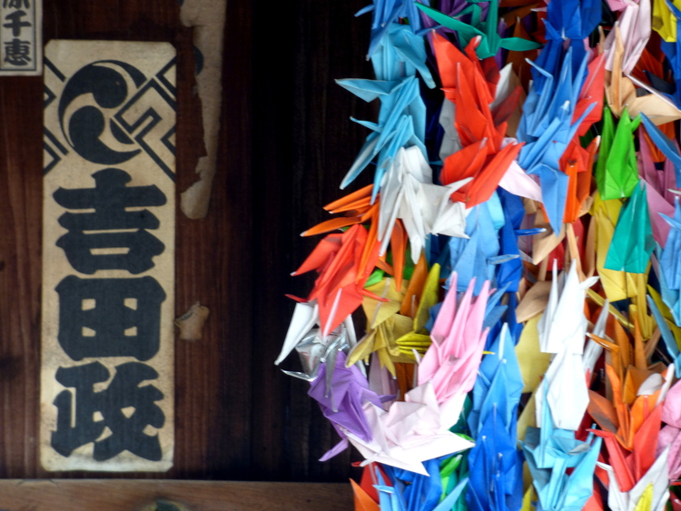 Strings of origami cranes in various colours next to some Japanese writing