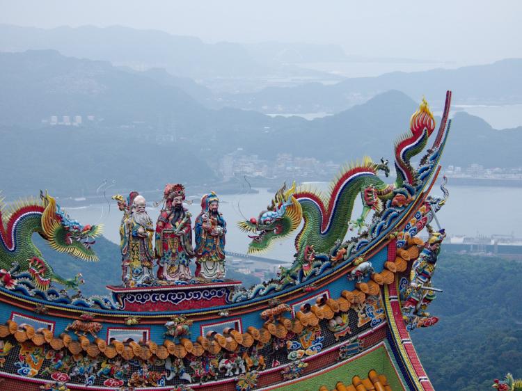 Colourful statues depicting three people and two Chinese dragons on the roof of a shrine