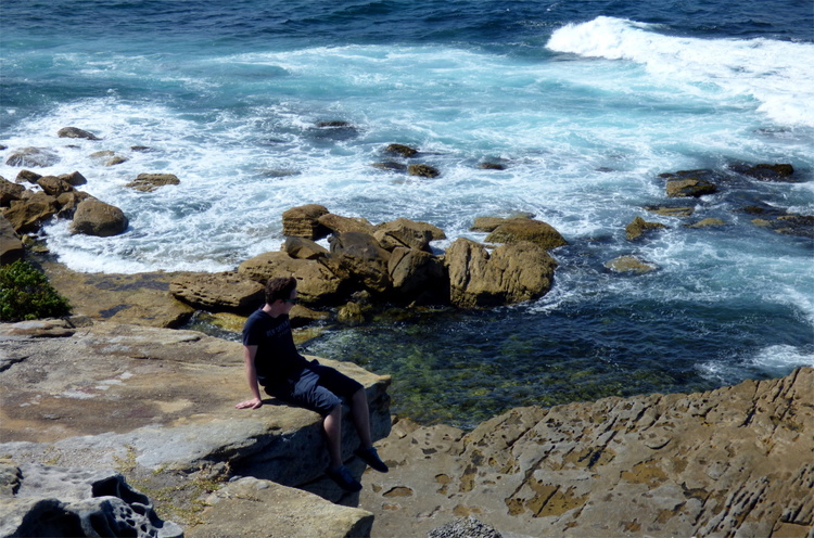 Jan sitting with his feet dangling of a rocky cliff above the ocean