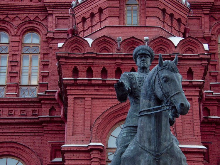 Statue of a horseback rider extending the palm of his hand towards the camera in front of an intricate red brick building