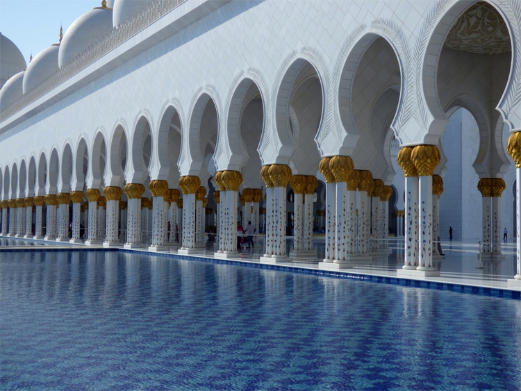 A shallow decorative pool in front of a passageway with white-and-gold arches and columns to either side
