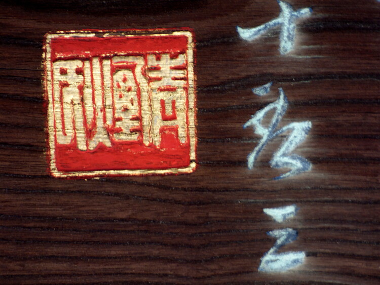 Close-up of a wooden surface with a red stamp and white Japanese characters engraved in it