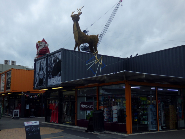 A large deer figure standing on a building complex made from grey and orange painted shipping containers housing various shops