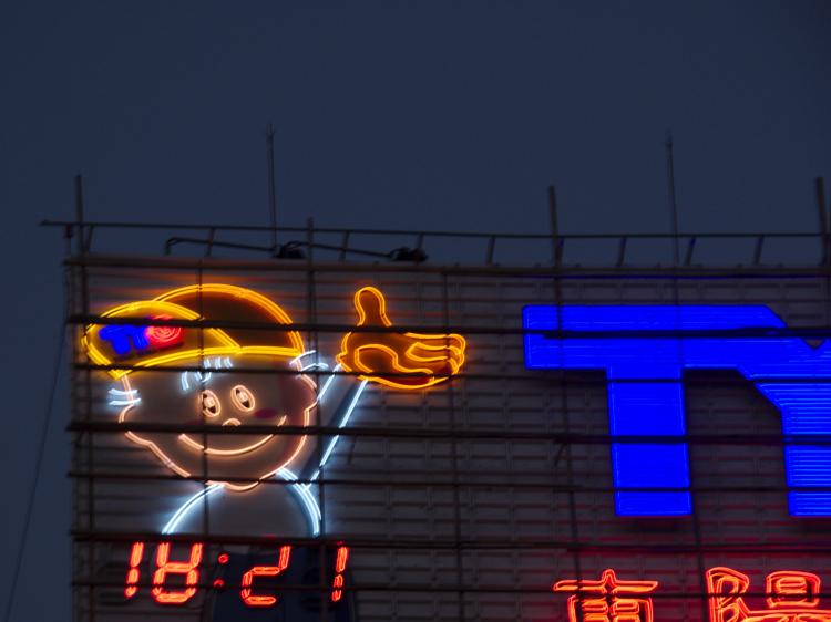 A large neon sign showing a cartoon-illustration of a boy in a baseball cap extending his hand