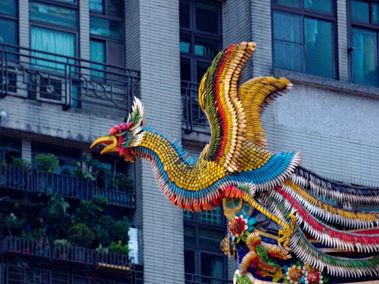 A sculpture of a phoenix taking flight on the roof of a temple made of colourful clay tiles