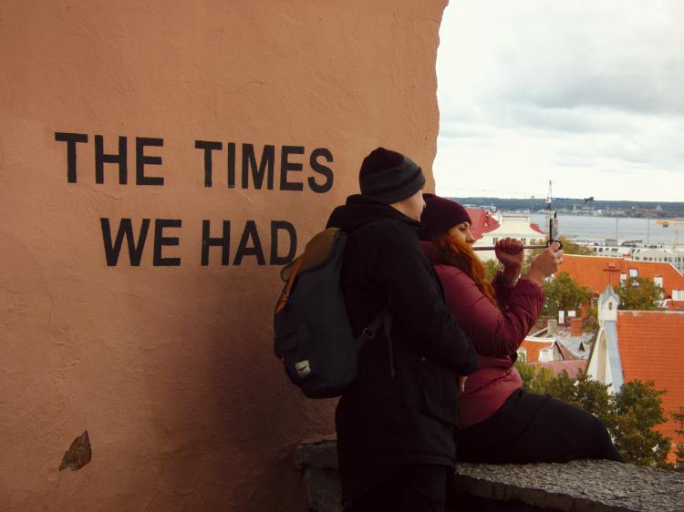 A couple taking selfies in front of a red wall with the words 'The Times We Had' written on it in large black letters