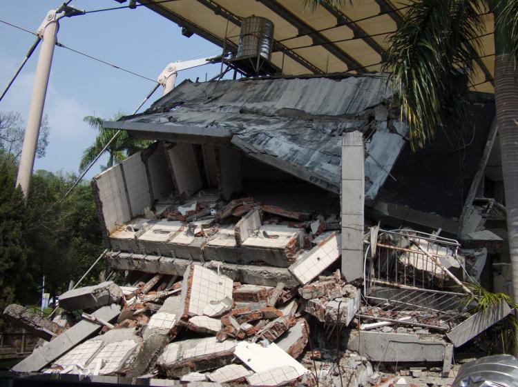 A collapsed school building under a metal roof construction with pieces of rubble spilling out from the remains of the building