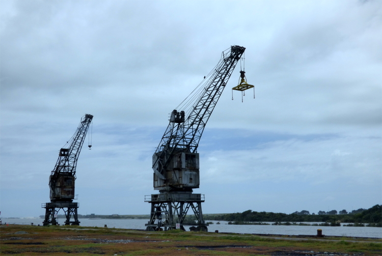 Two rusty abandoned loading cranes on a riverside