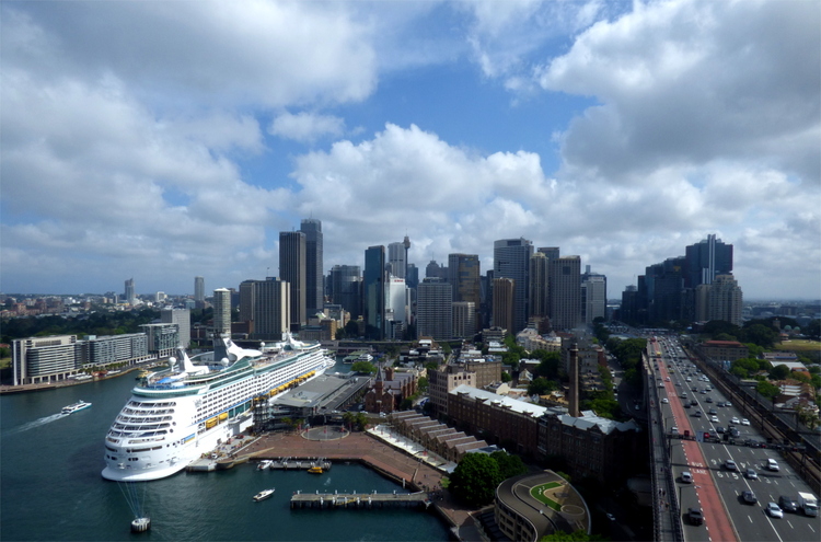 A view of the Sydney harbour with a large cruise ship in front of a skyline in the distance