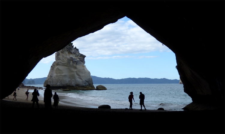 Silhouettes of people walking on a beach seen through the opening of a cave