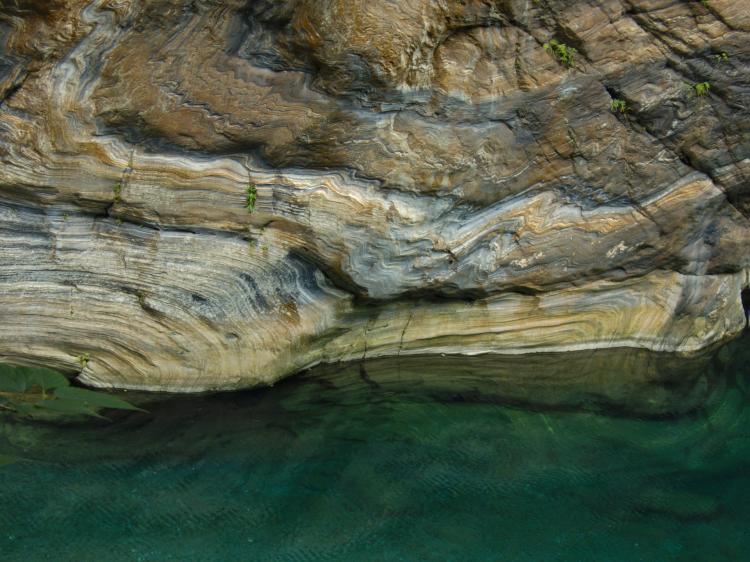 Folded layers of sediment in various colours above a turquoise river
