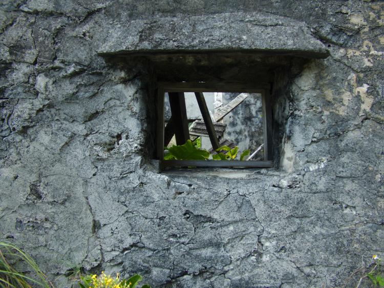 A window in a rough stone wall showing the inside of an abandoned house
