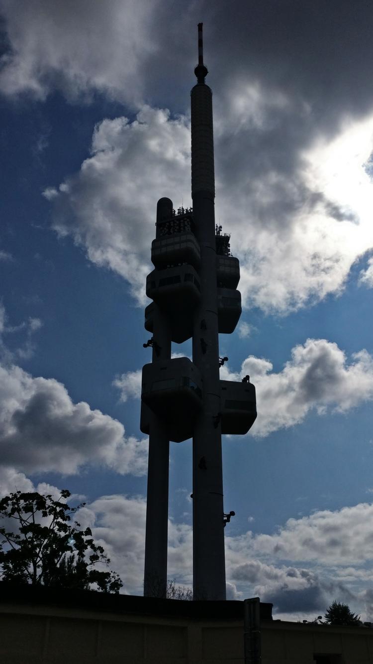 The silhouette of a tall modernist television tower with many sculptures of babies mounted to its sides that look like ants crawling up the tower