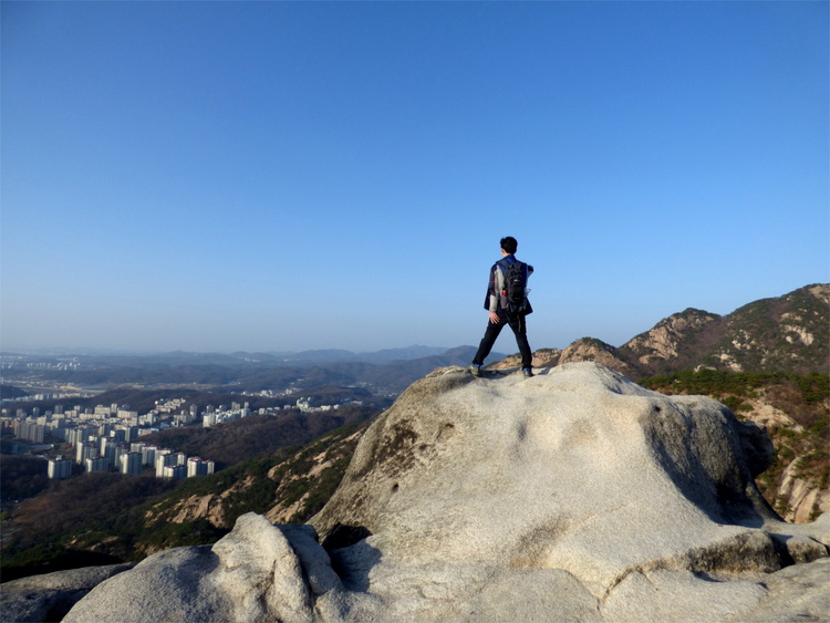 A man standing on a rock formation looking at the city below the mountain