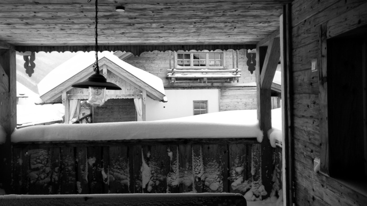 A snow-covered wooden terrace in black and white with a hooded glass lamp hanging from the ceiling