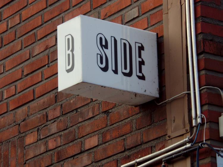 A cubic white lamp on a red brick wall reading 'B SIDE'