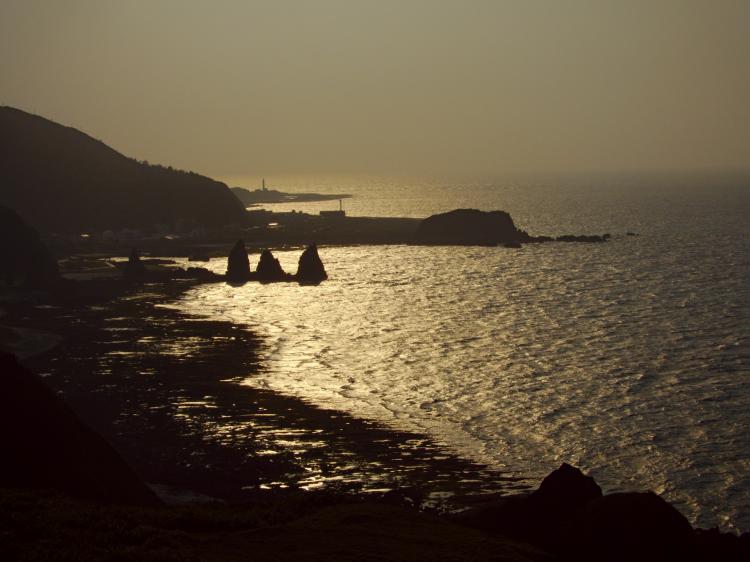 Golden sunlight reflecting off the rough sea on a rocky, monochrome shoreline