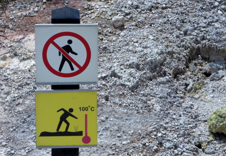 A sign featuring a human figure in a strike-through circle as well as a figure walking on rocky ground with a thermometer reading '100° C' beside it