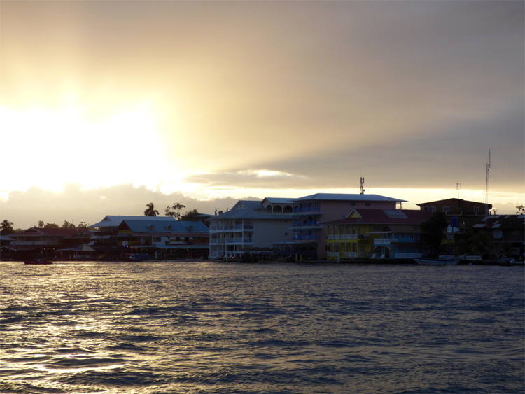 A row of pastel-coloured houses built into a waterfront, seen from the water with a sunset sky in the background