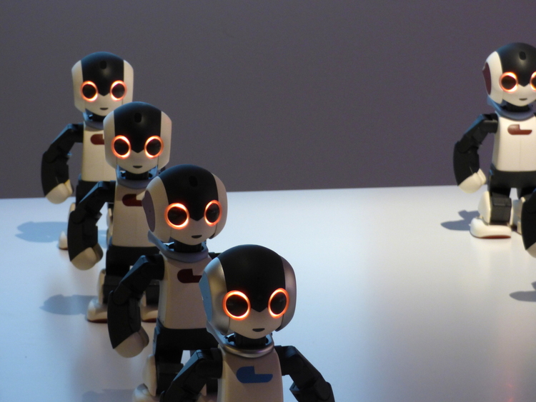 A row of humanoid toy robots with glowing orange eyes standing on a plain white surface