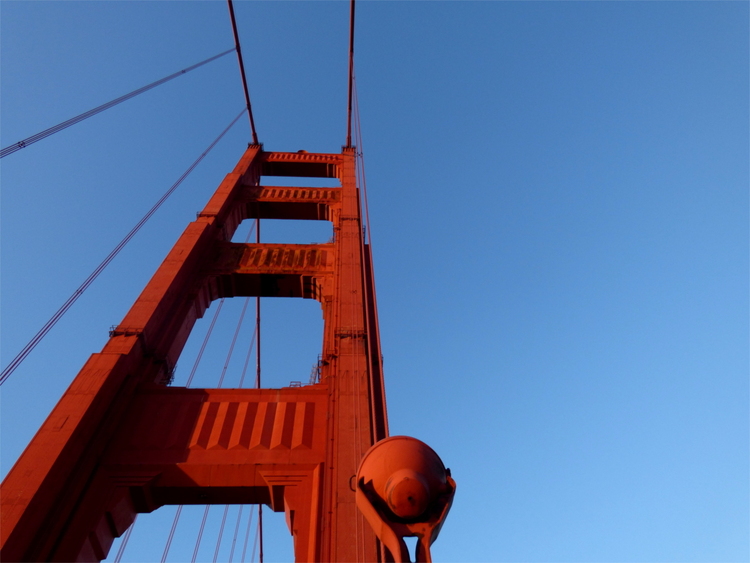 A look up towards one of the red gates of the Golden Gate bridge in front of a light blue sky