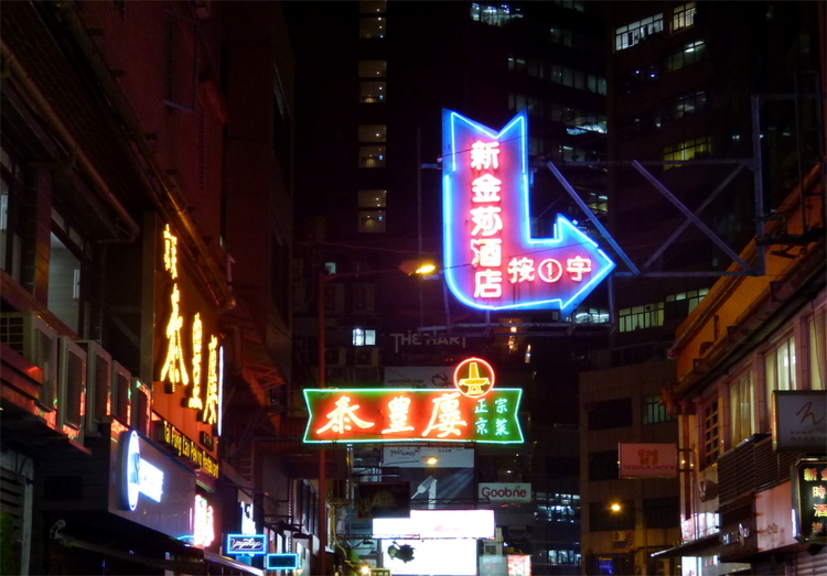 Large, multi-coloured neon signs with Chinese writing suspended above a street