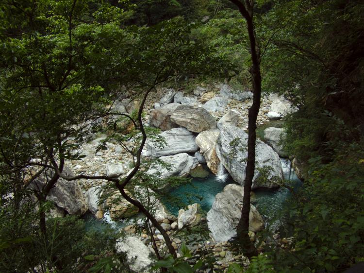 View of a deep blue river running past large rocks, seen through some trees