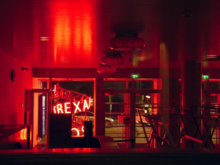 Interiour of an empty cafe flooded by red light from a neon sign outside the window